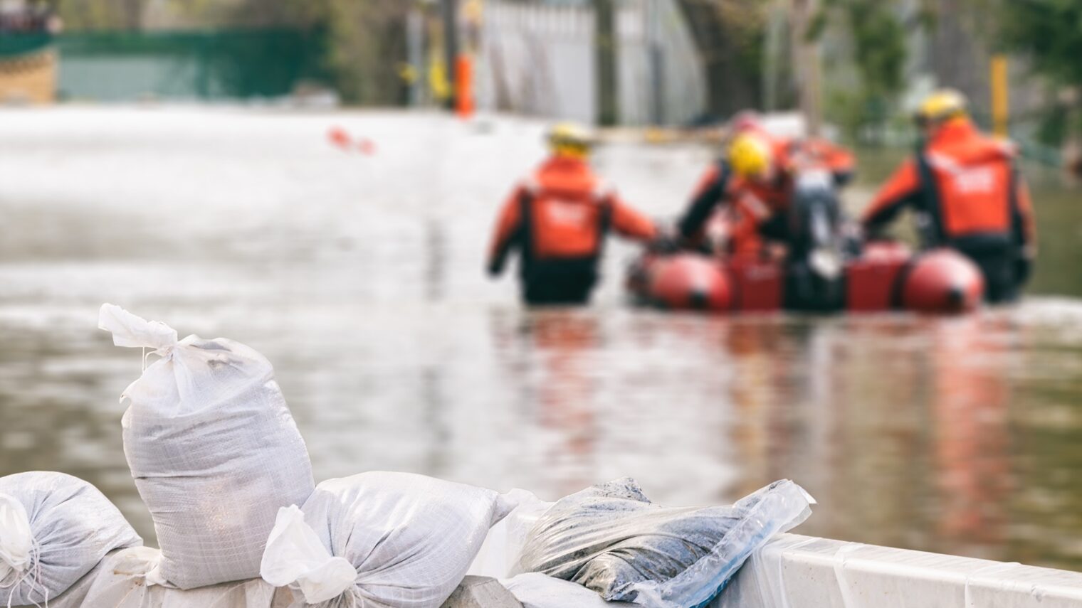 Rettungskräfte mit Rettungsboot beim Hochwasser-Einsatz. Im Vordergrund Sandsäche.