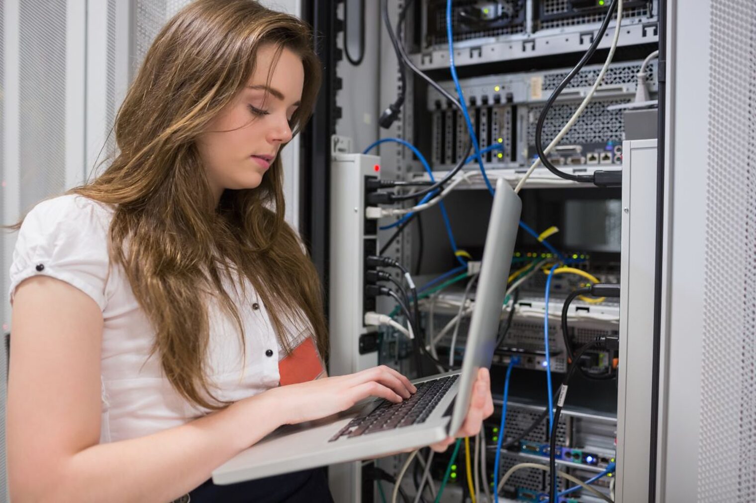 Junge Frau, die Laptop verwendet, um auf Servern im Rechenzentrum zu arbeiten.