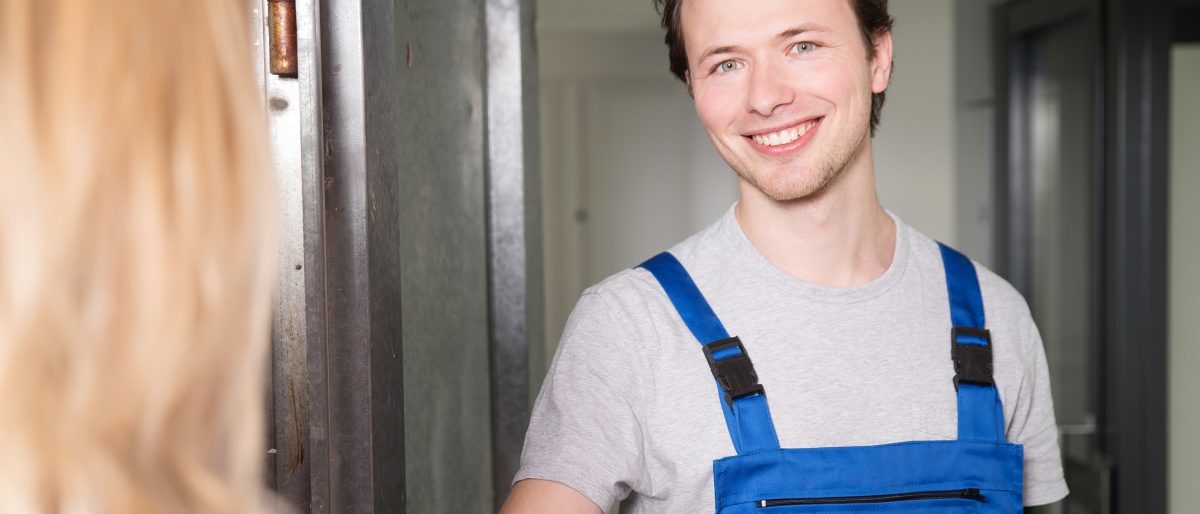 Handwerker im Blaumann begrüßt Kundin
