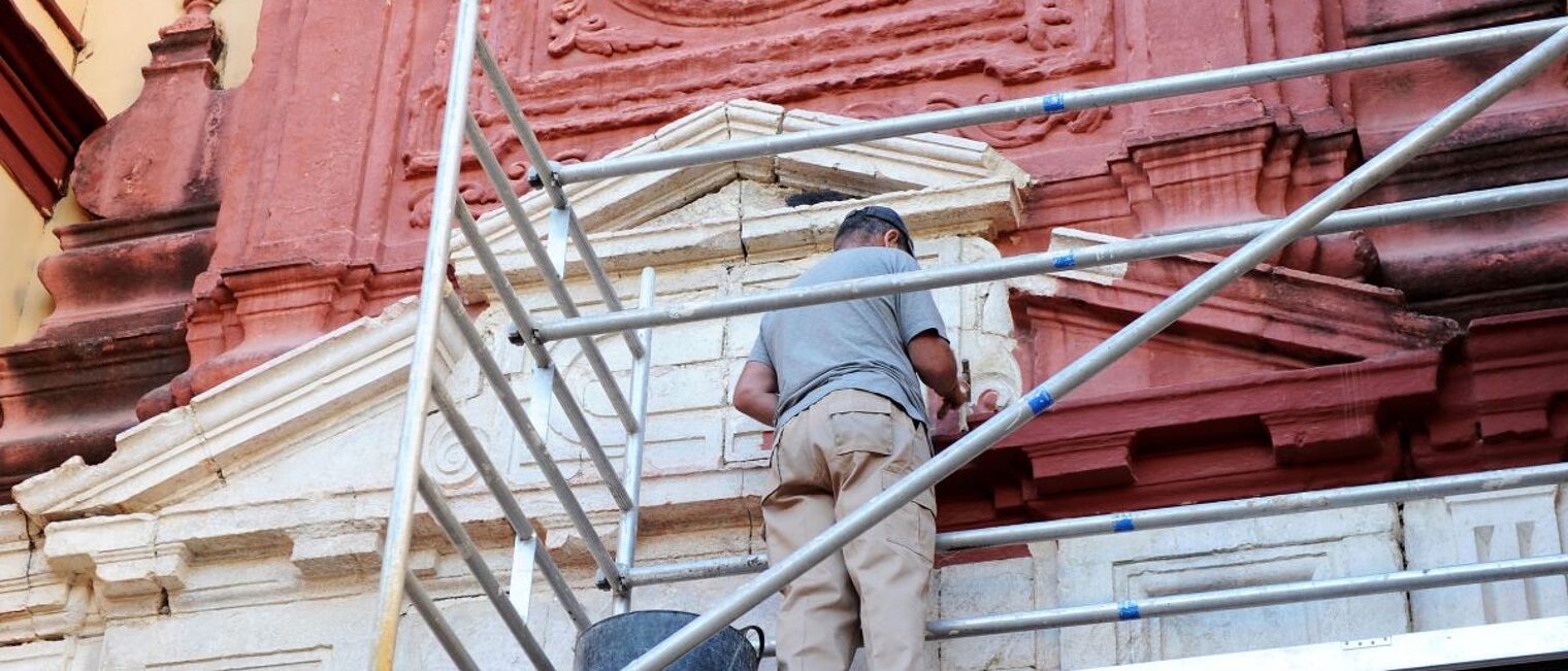 Denkmalpflege, Restaurierung. Mann auf Gerüst restauriert Fassade einer Kirche.