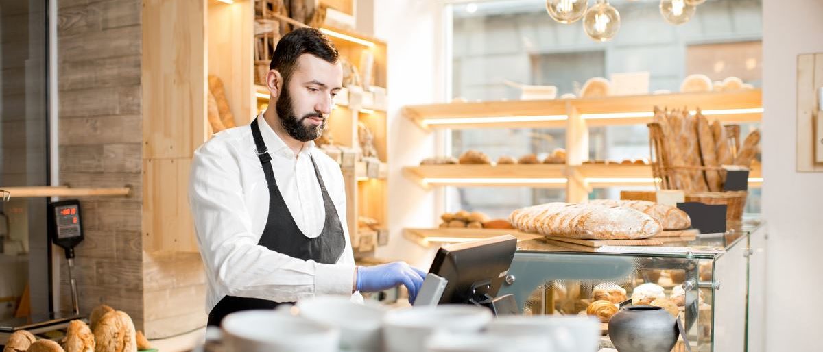 Bäckerei-Verkäufer gibt Geldbetrag in Kassensystem ein. Bäckerei-Verkäufer gibt Geldbetrag in Kassensystem ein.