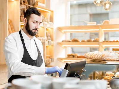Bäckerei-Verkäufer gibt Geldbetrag in Kassensystem ein. Bäckerei-Verkäufer gibt Geldbetrag in Kassensystem ein.