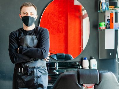 Friseur in seinem Salon mit Maske