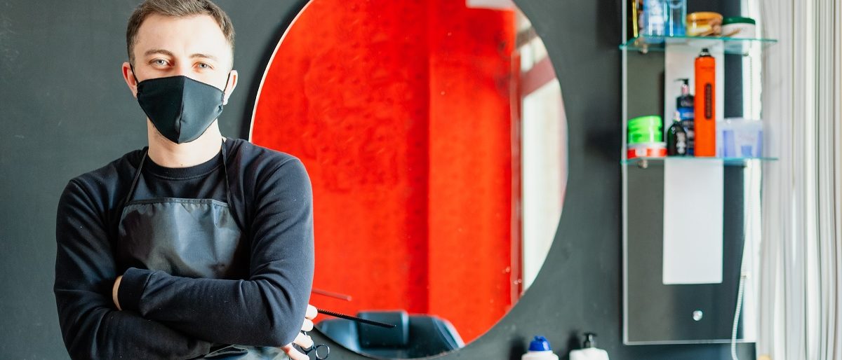 Friseur in seinem Salon mit Maske