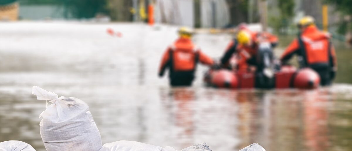 Rettungskräfte mit Rettungsboot beim Hochwasser-Einsatz. Im Vordergrund Sandsäche.