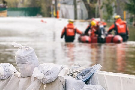 Rettungskräfte mit Rettungsboot beim Hochwasser-Einsatz. Im Vordergrund Sandsäche.