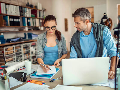 Mann und Frau im Büro vor einem Laptop in einem Gespräch