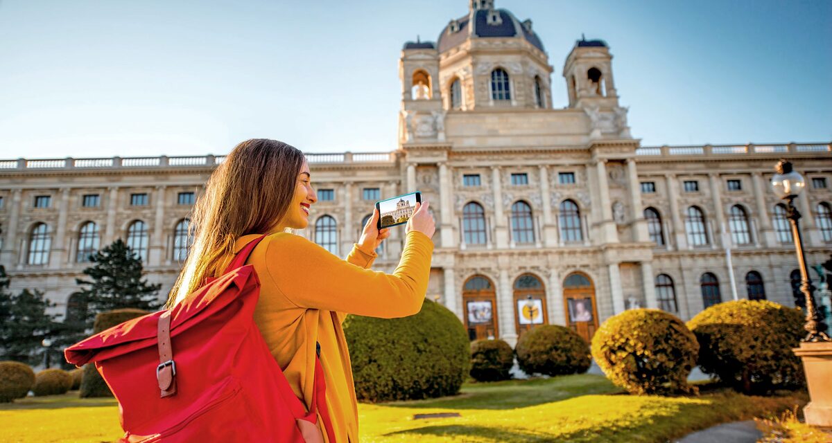 Junge Frau mit Rucksack fotografiert die Wiener Hofburg mit ihrem Handy.