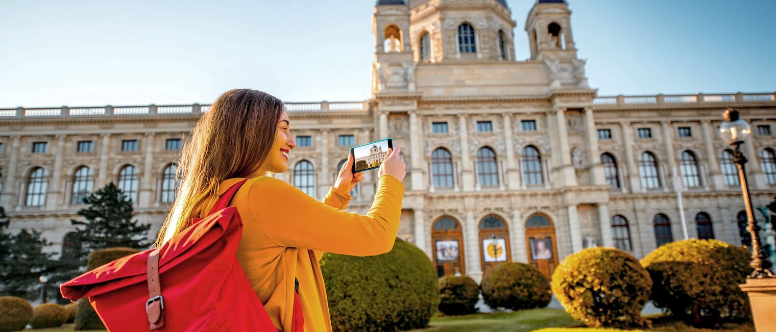 Junge Frau mit Rucksack fotografiert die Wiener Hofburg mit ihrem Handy.