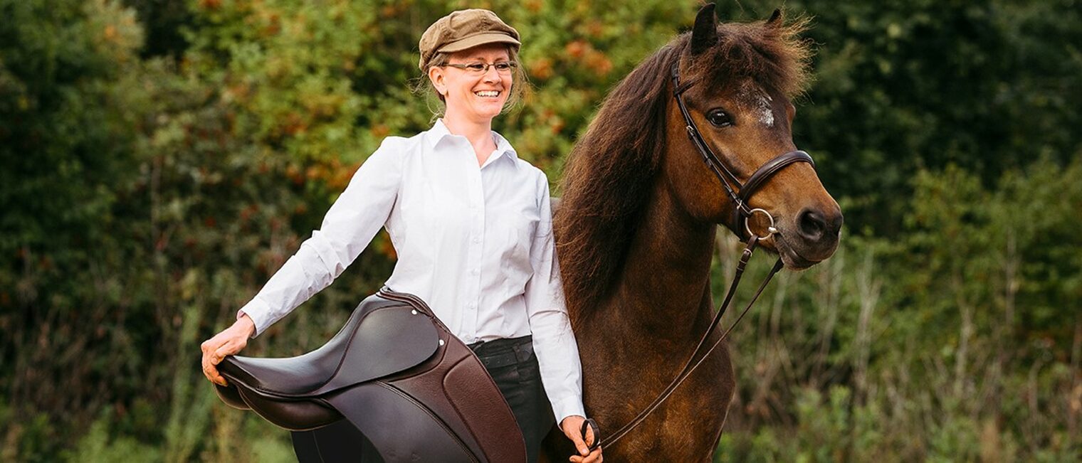 Portrait von Meike Klein mit einem Sattel auf dem Arm und neben einem Pony.
