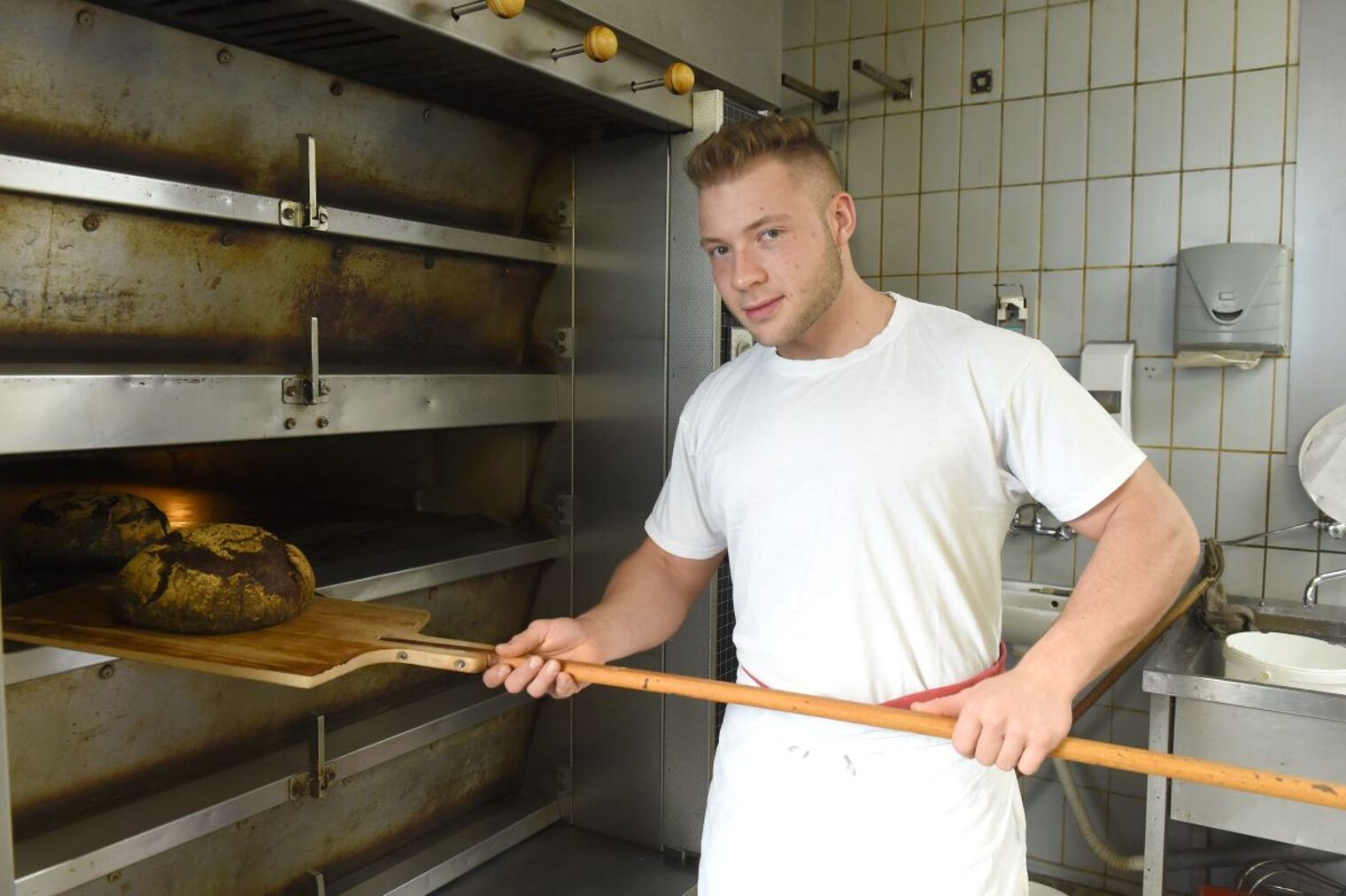 Bäcker Schall schiebt ein Brot in den Backofen.