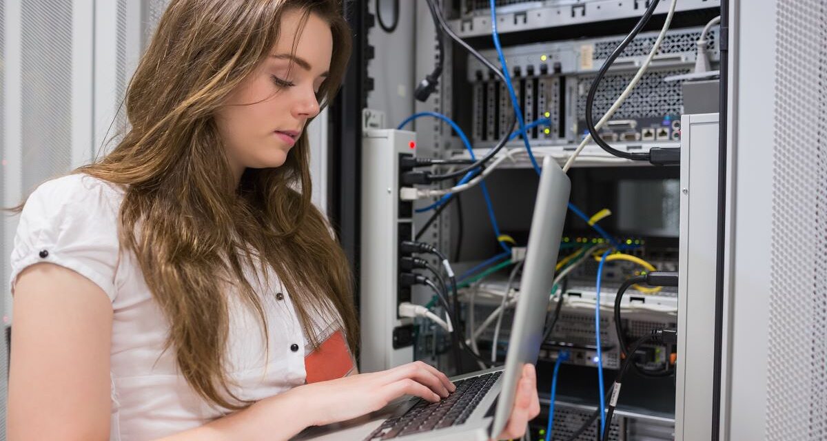 Junge Frau, die Laptop verwendet, um auf Servern im Rechenzentrum zu arbeiten.