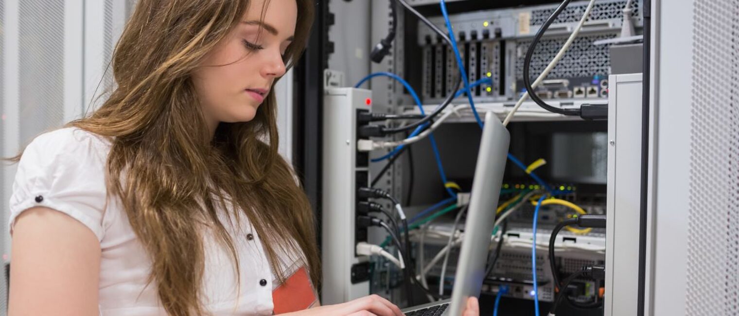 Junge Frau, die Laptop verwendet, um auf Servern im Rechenzentrum zu arbeiten.