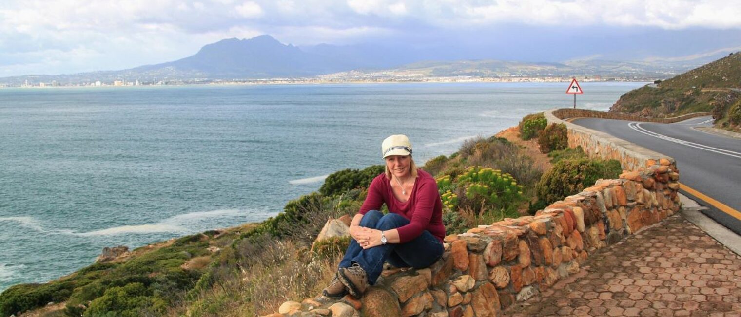 Junge Frau sitzt auf Steinmauer an der Bucht von Kapstadt.