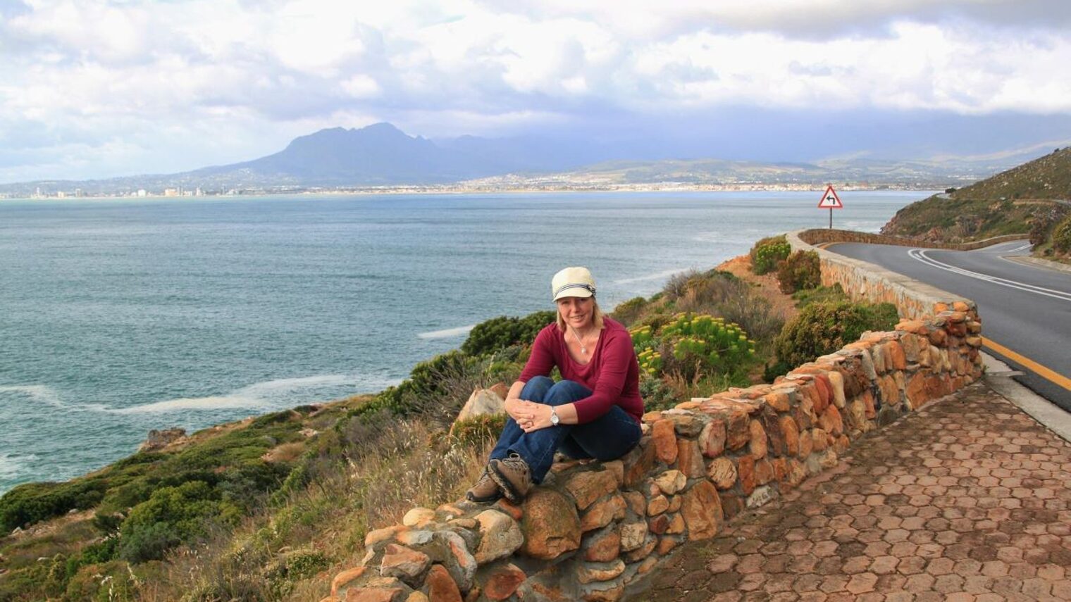 Junge Frau sitzt auf Steinmauer an der Bucht von Kapstadt.