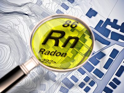Eine Lupe zeigt einen Ausschnitt aus Periodensystem mit dem Element Radon auf dem Hintergrund eines Stadtplanes.