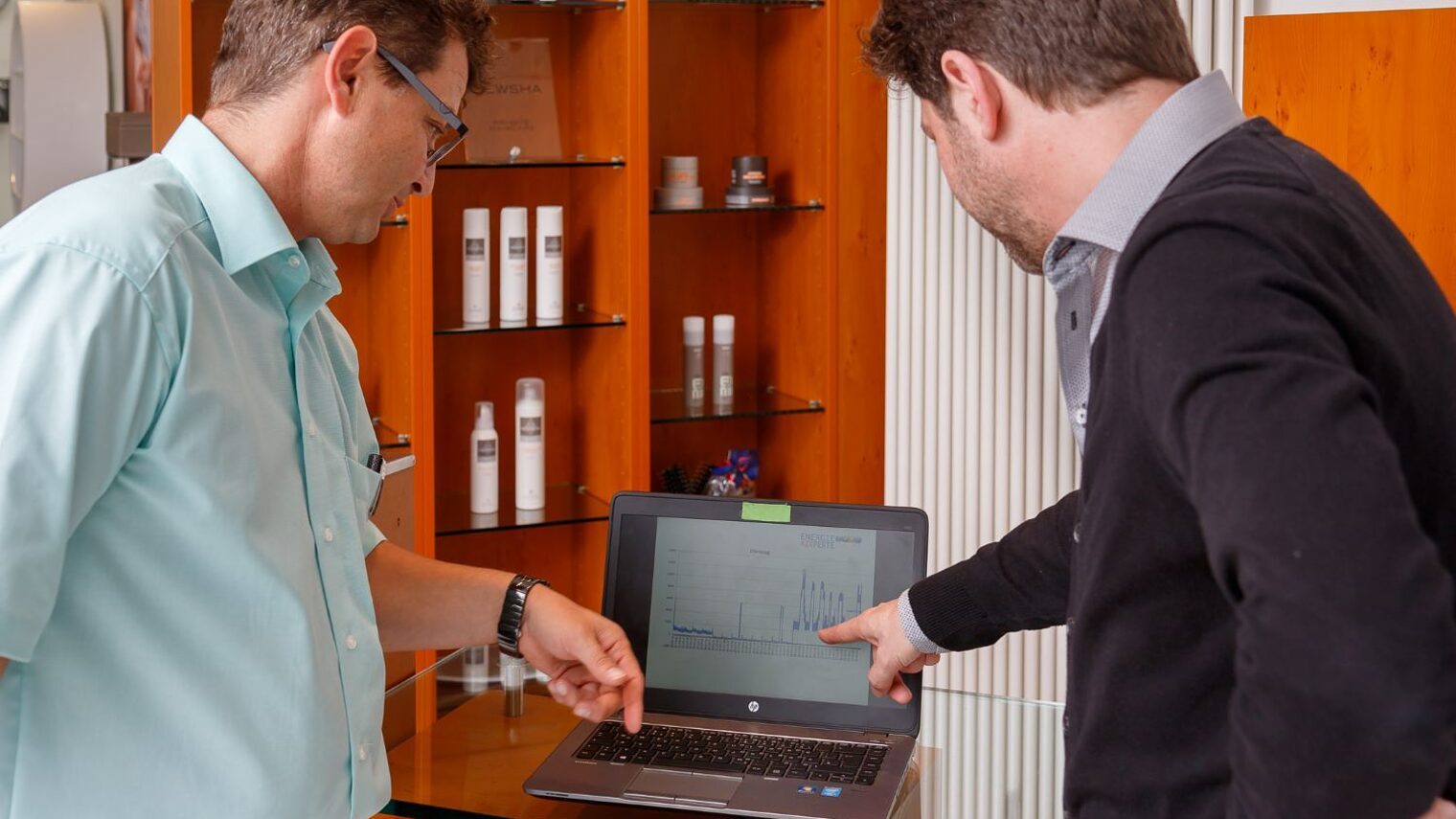 Ein Energieexperte zeigt einem Friseursalon-Inhaber an einem Laptop den Energieverbraucht.