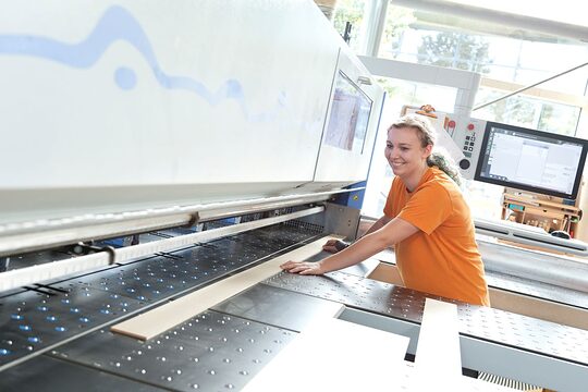 Tischlerin sägt ein Brett an der Maschine zurecht.