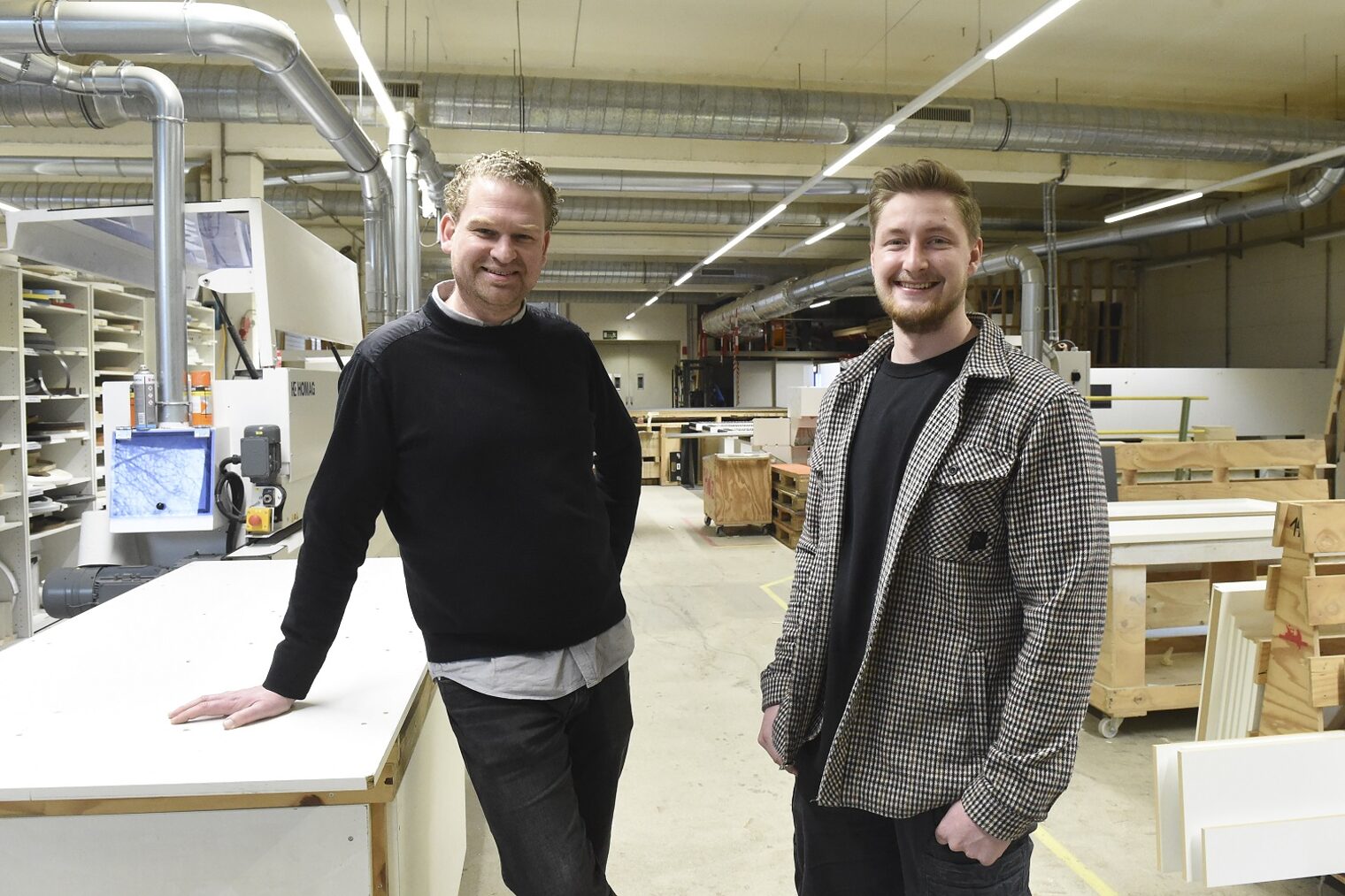 Geschäftsführer und Mitarbeiter einer großen Tischlerei stehen zusammen in der Werkstatt.