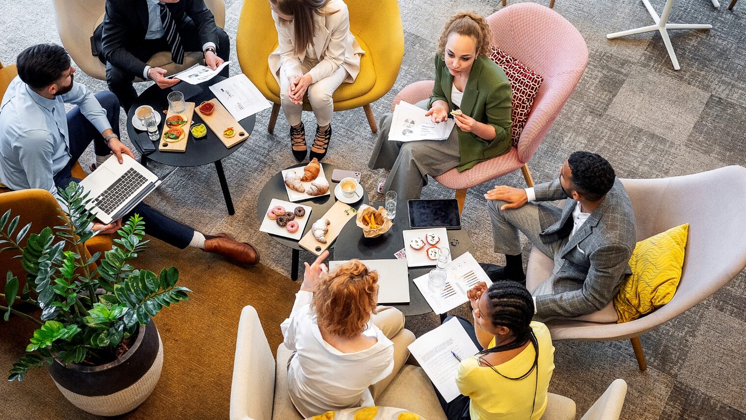 Junge Geschäftsleute oder Kollegen sitzen zu einem Arbeitsgespräch zusammen und haben Frühstück oder Lunch.