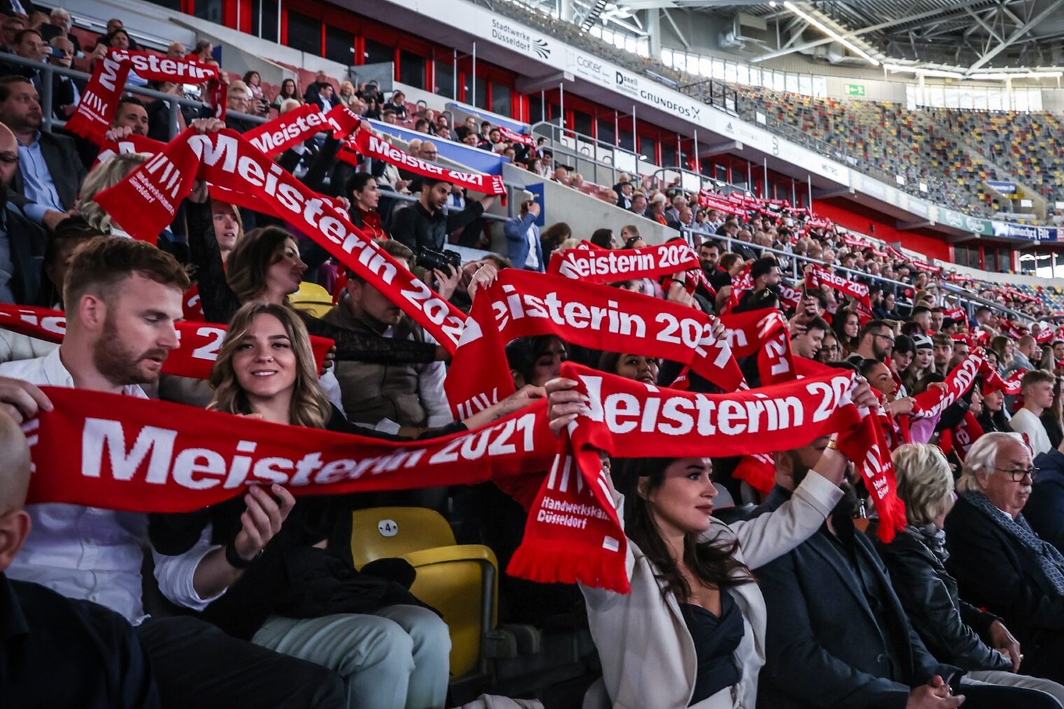 Meisterinnen und Meister halten auf der Tribüne ihre Meisterschals hoch.