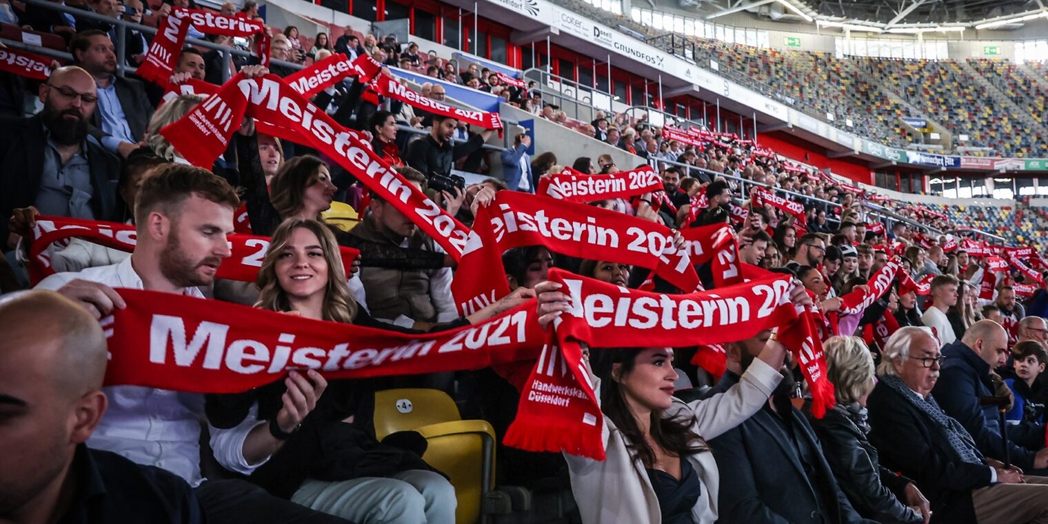 Meisterinnen und Meister halten auf der Tribüne ihre Meisterschals hoch.