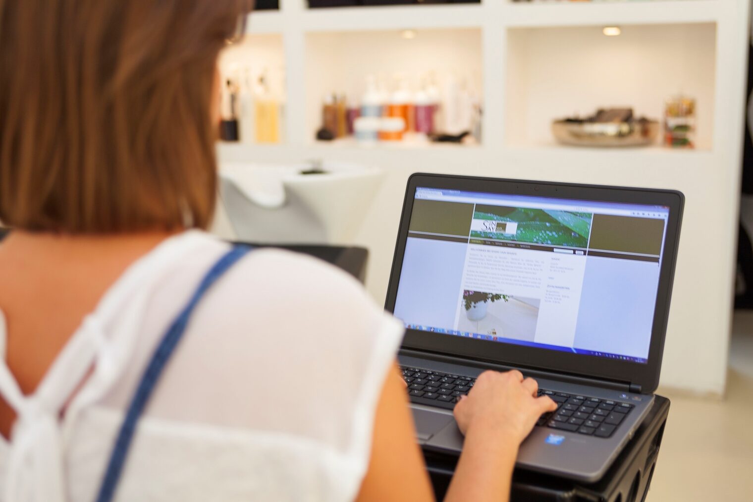 Rückenansicht einer Friseurinhaberin, die an ihrem Laptop arbeitet.