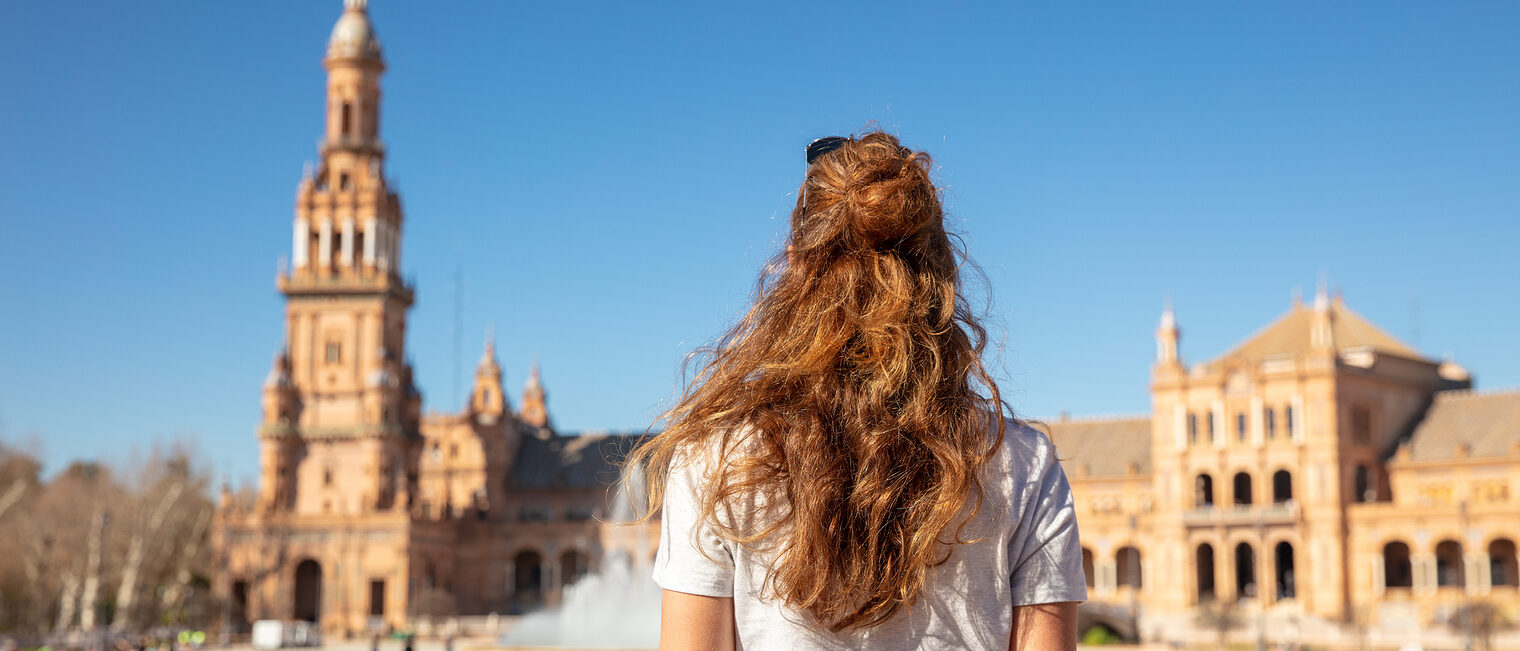 Rückenansicht einer jungen Frau, die auf der Plaza de Espana in Sevilla steht.