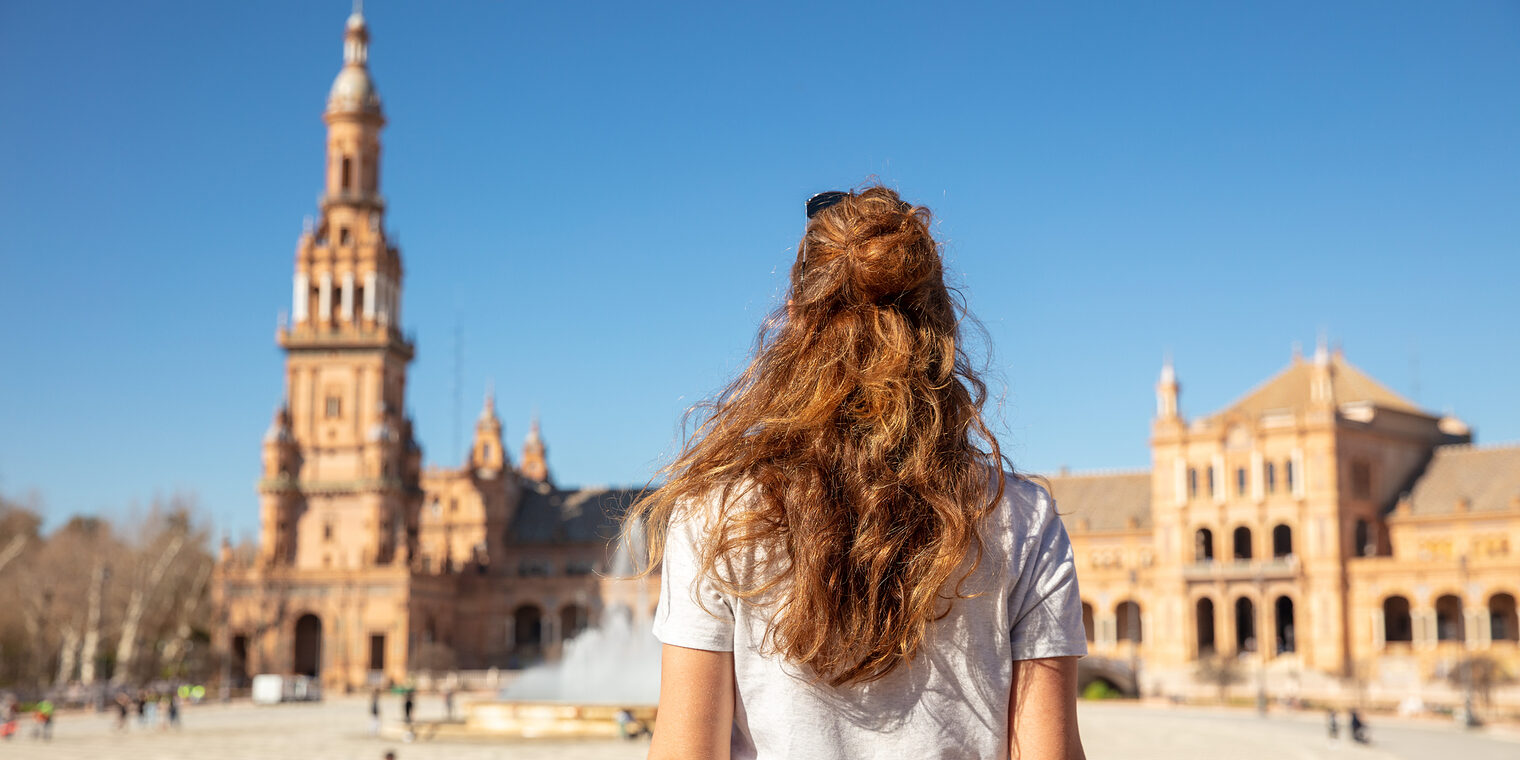 Rückenansicht einer jungen Frau, die auf der Plaza de Espana in Sevilla steht.