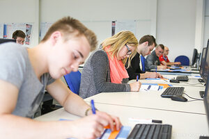 Teilnehmer eines Seminars schreiben Notizen an Computertischen