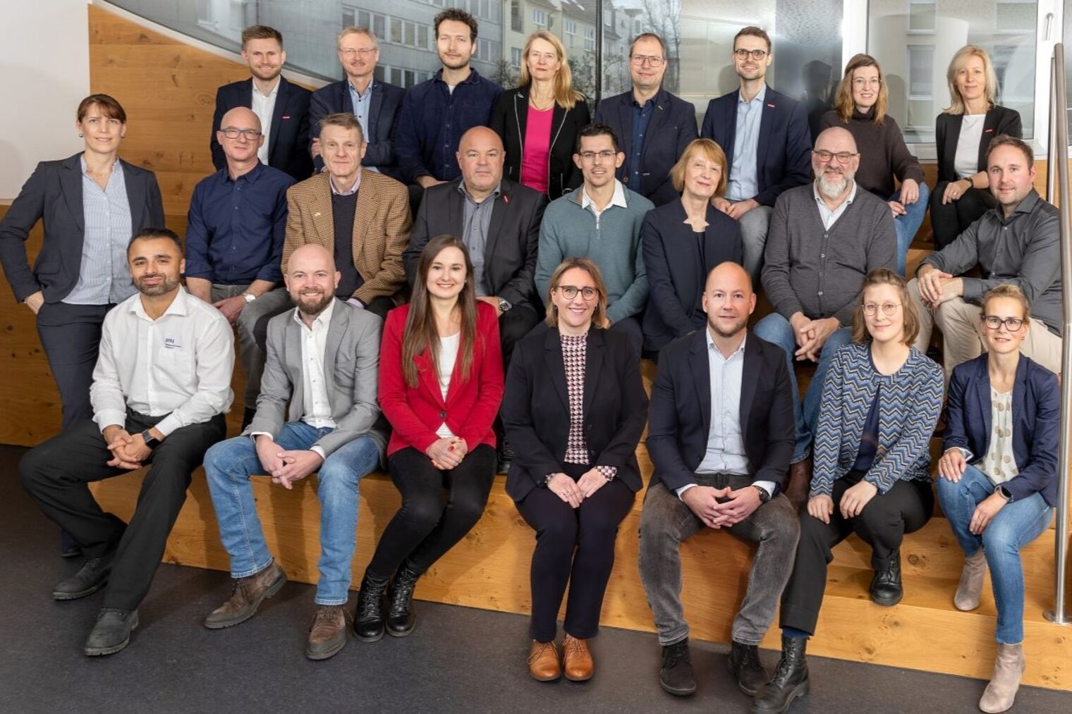 Das Team der Betriebsberatung in drei Reihen auf einer Holztreppe