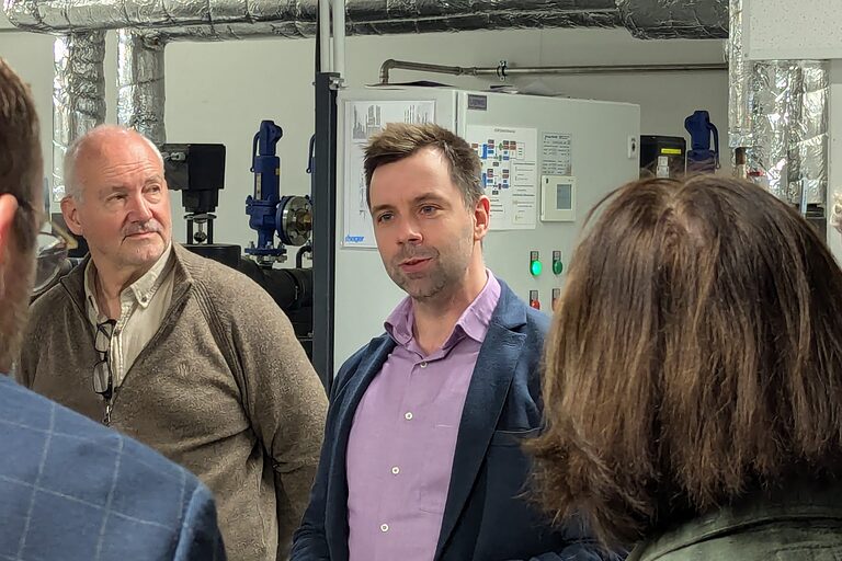 Der Projektleiter Dennis Scharbert steht mittig im Bild. Um ihn herum stehen drei weitere Personen. 