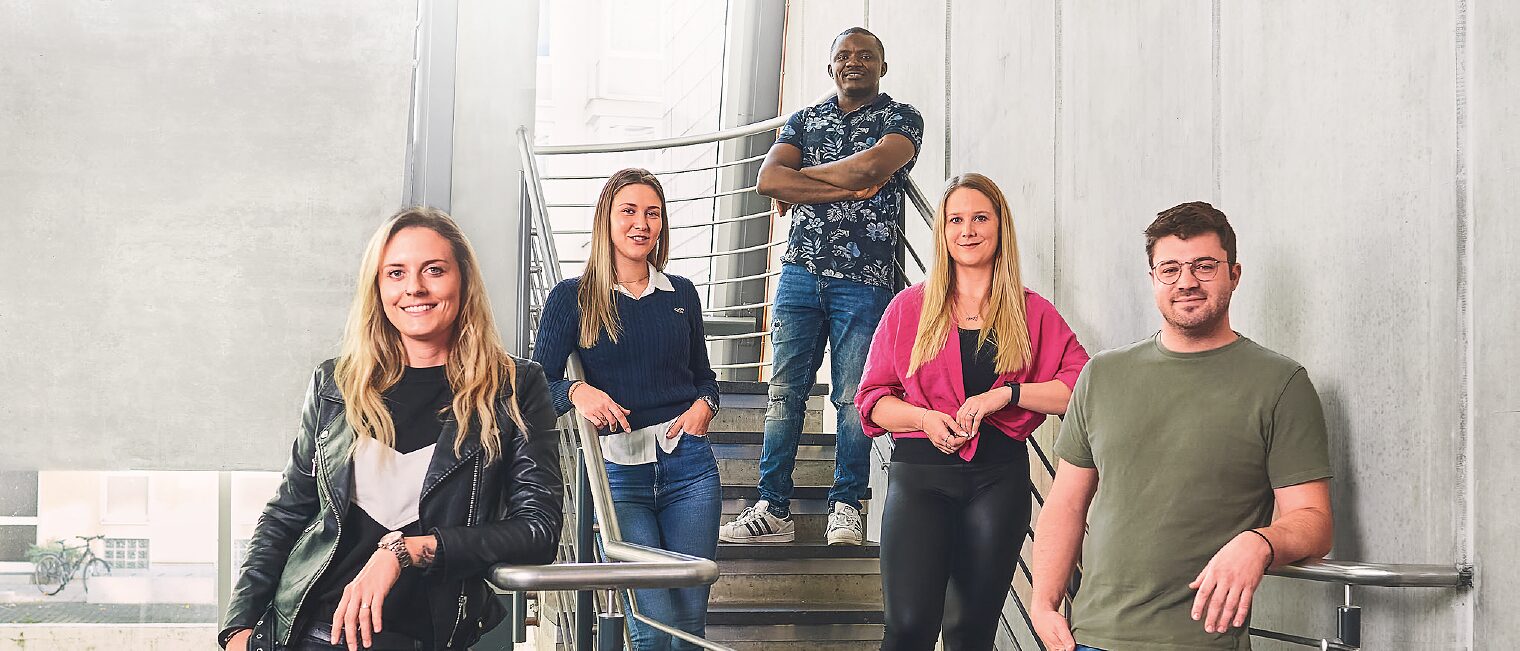 5 Meisterschülerinnen und -schüler stehen im Treppenhaus auf Stufen und ans Geländer gelehnt