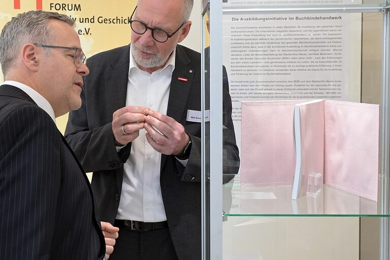 ZDH-Präsident Jörg Dittrich und Maik Beckmann vom BDBI beim Betrachten von Ausstellungsstücken in einer Vitrine