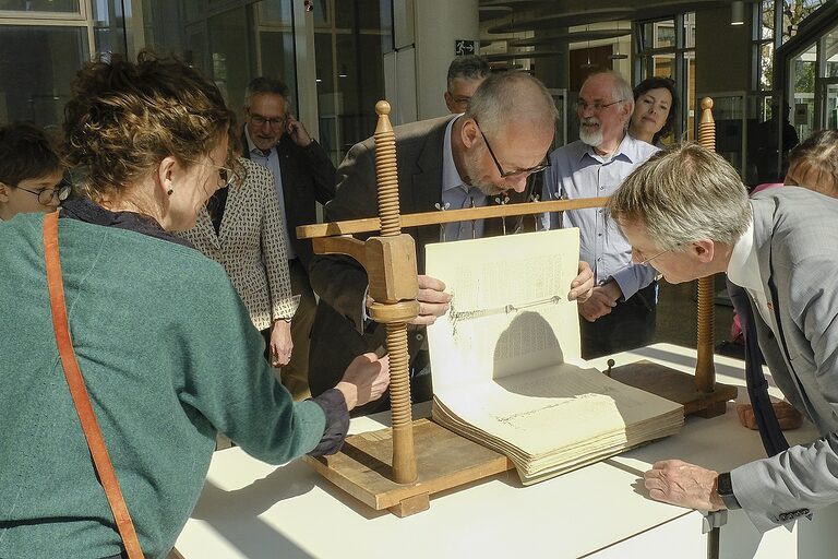 Maik Beckmann zeigt vor umstehenden Personen die Fadenheftung von Papierlagen in einer Heftlade