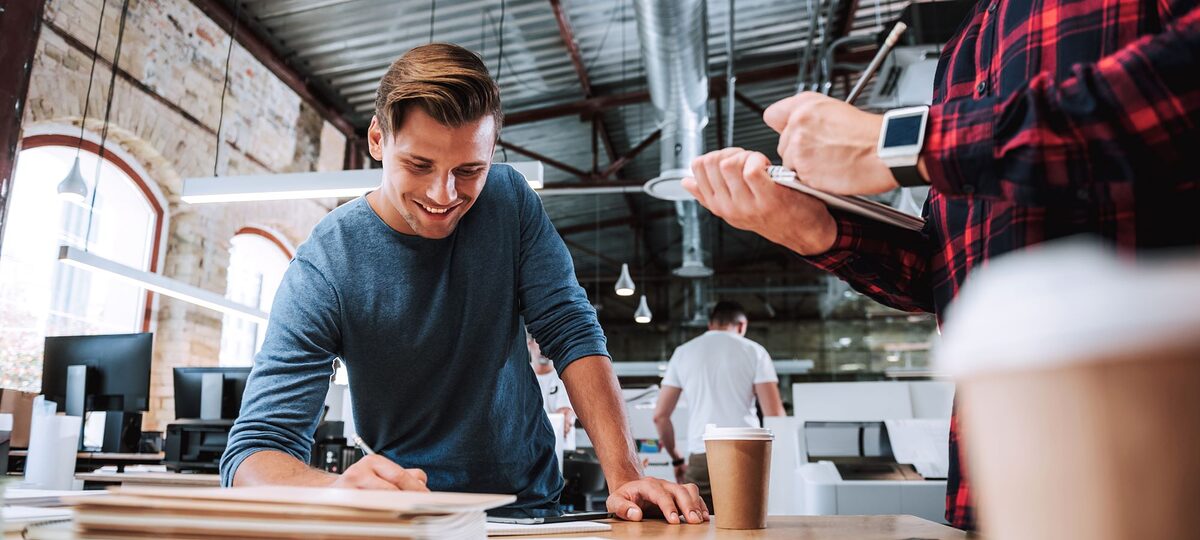 Zwei junge Männer machen Berechnungen im Notizbuch, die für ihre Arbeit notwendig sind, und lächeln