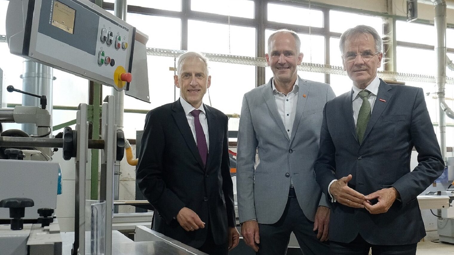 Die Teilnehmenden posieren vor einer Maschine im Tischlereibetrieb von Thomas Klode.