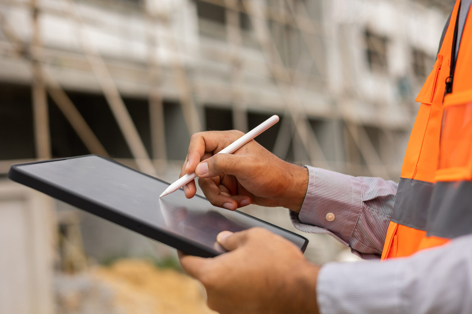 Nahaufnahme eines Ingenieurs, der mit dem Tablet arbeitet. Im Hintergrund eine Gebäude-Baustelle.