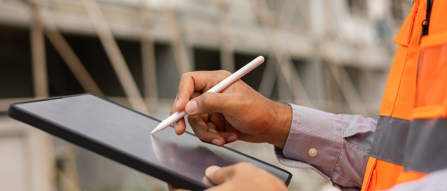 Nahaufnahme eines Ingenieurs, der mit dem Tablet arbeitet. Im Hintergrund eine Gebäude-Baustelle.