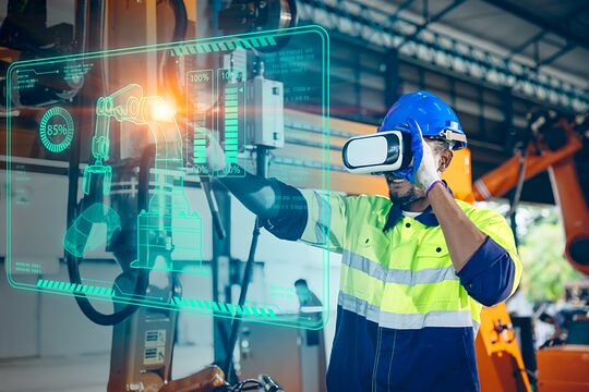 Männlicher Maschinenbauer mit VR-Brille bedient in Werkstatthalle eine Robotermaschine über eine virtuelle Wand.
