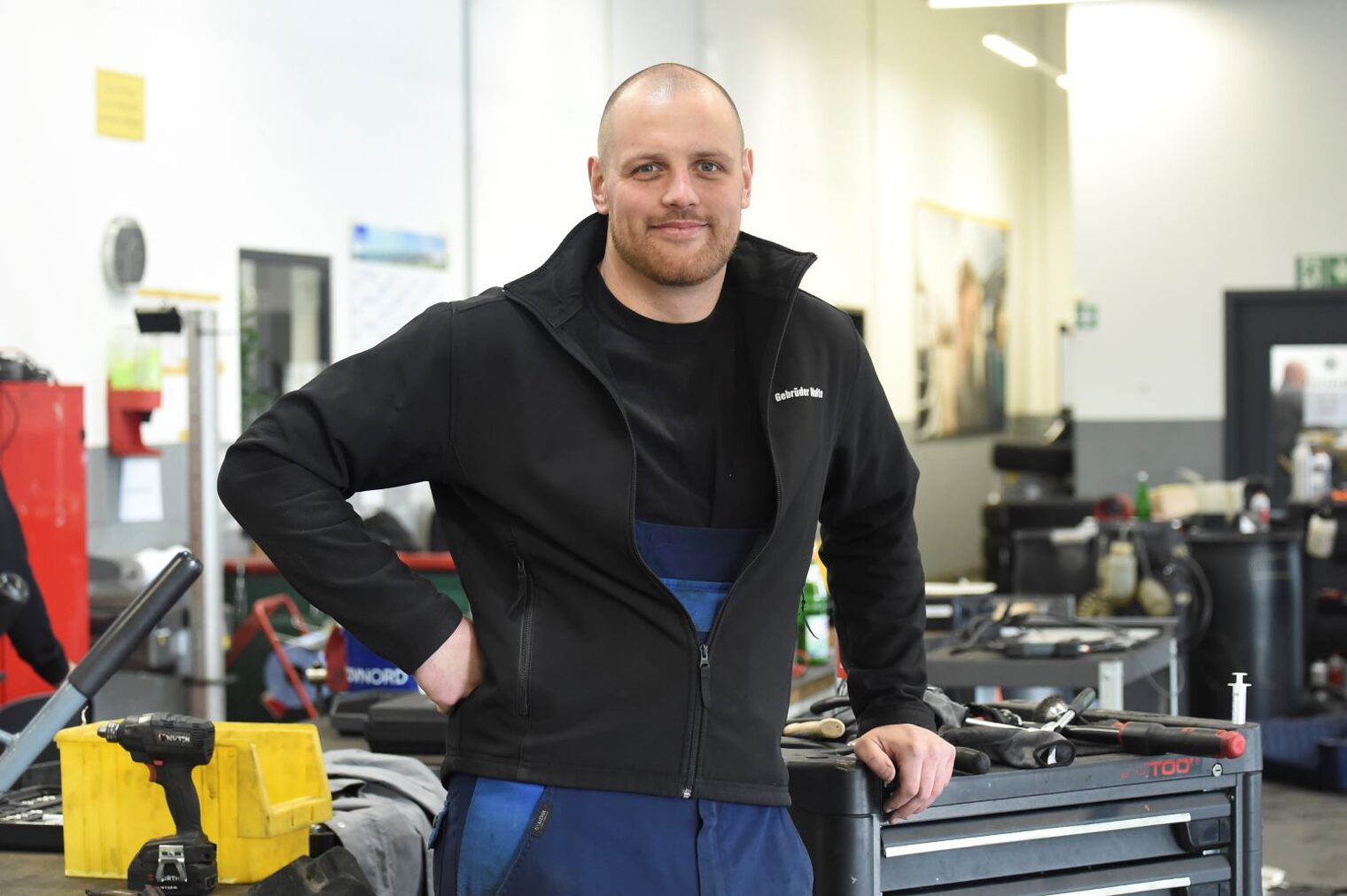 Sam Lindemann steht in einer Autowerkstatt und lehnt an einem Rollcontainer.