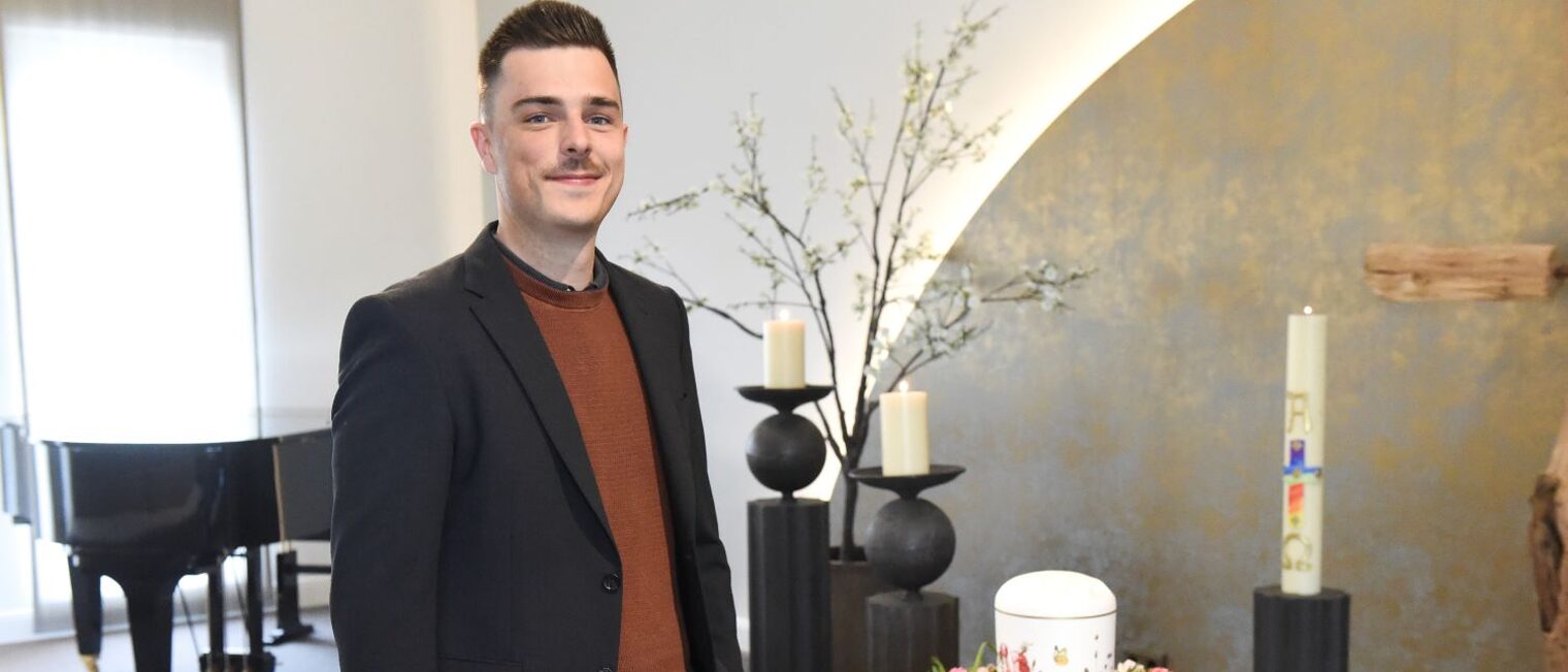Andreas Werner steht in einem Ausstellungsraum neben einer mit Blumen geschmückten Urne.