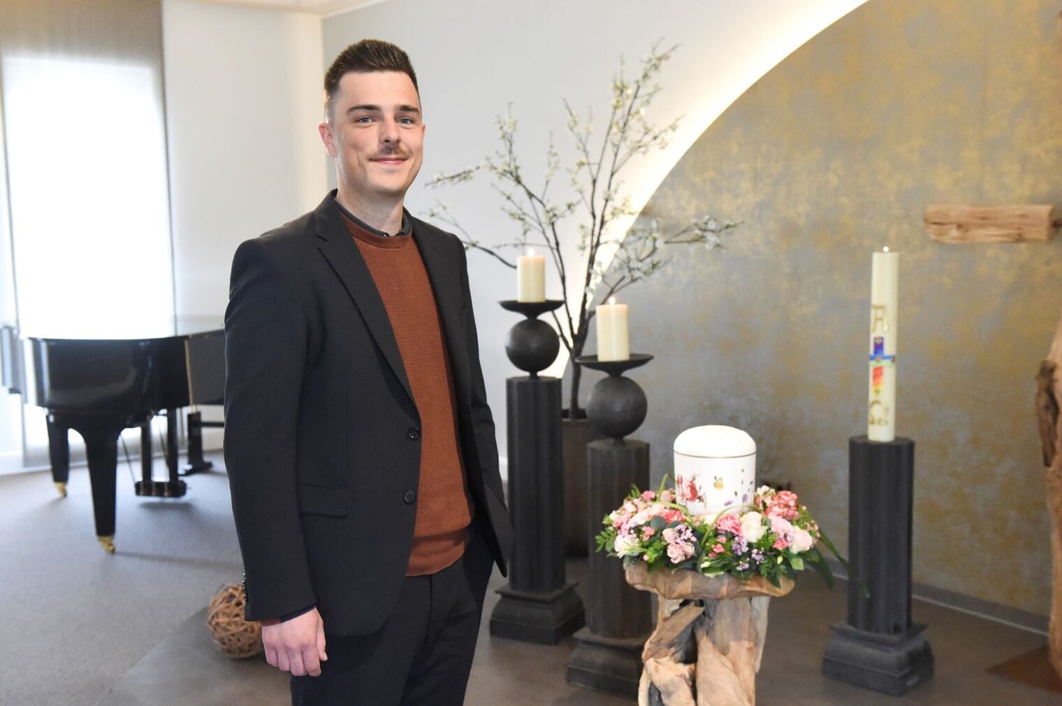Andreas Werner steht in einem Ausstellungsraum neben einer mit Blumen geschmückten Urne.