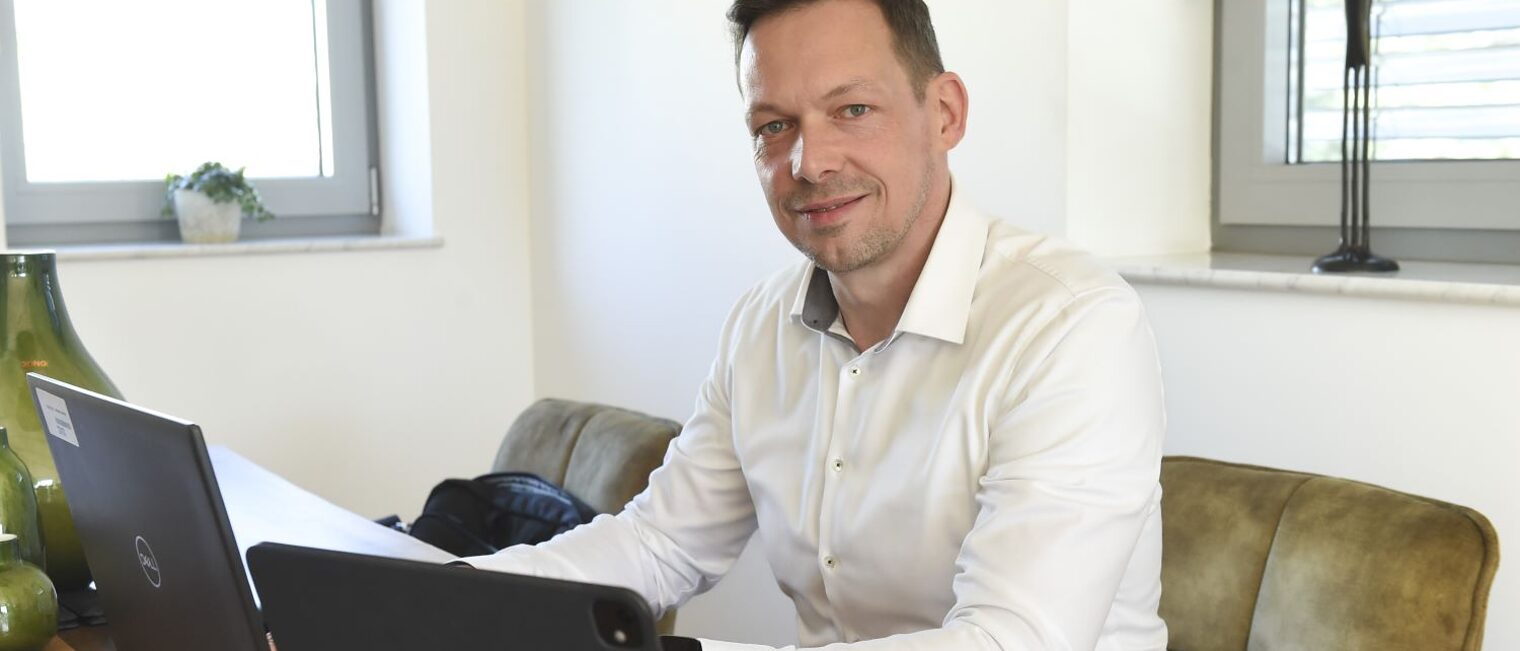 Andre Reichelt sitzt in seinem Büro an einem Schreibtisch. Vor ihm befinden sich zwei Laptops.