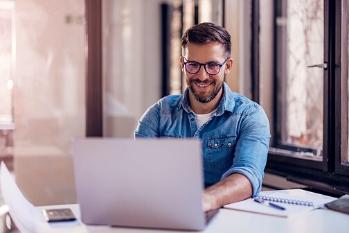 Lächelnder Geschäftsmann, der im Büro sitzt und am Laptop arbeitet.