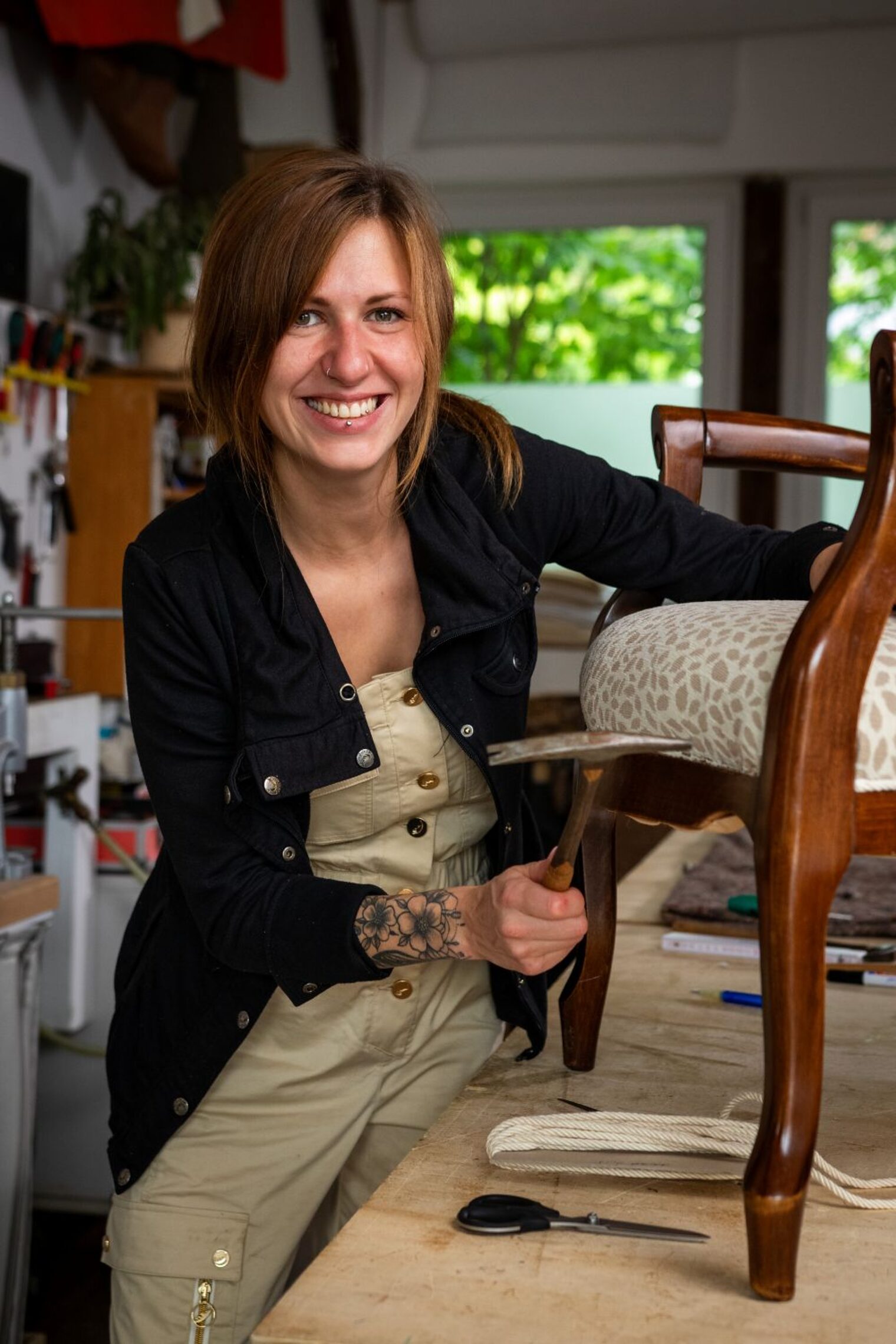 Anna-Lena Nissen arbeitet an der Polsterung eines Stuhles und lächelt in die Kamera