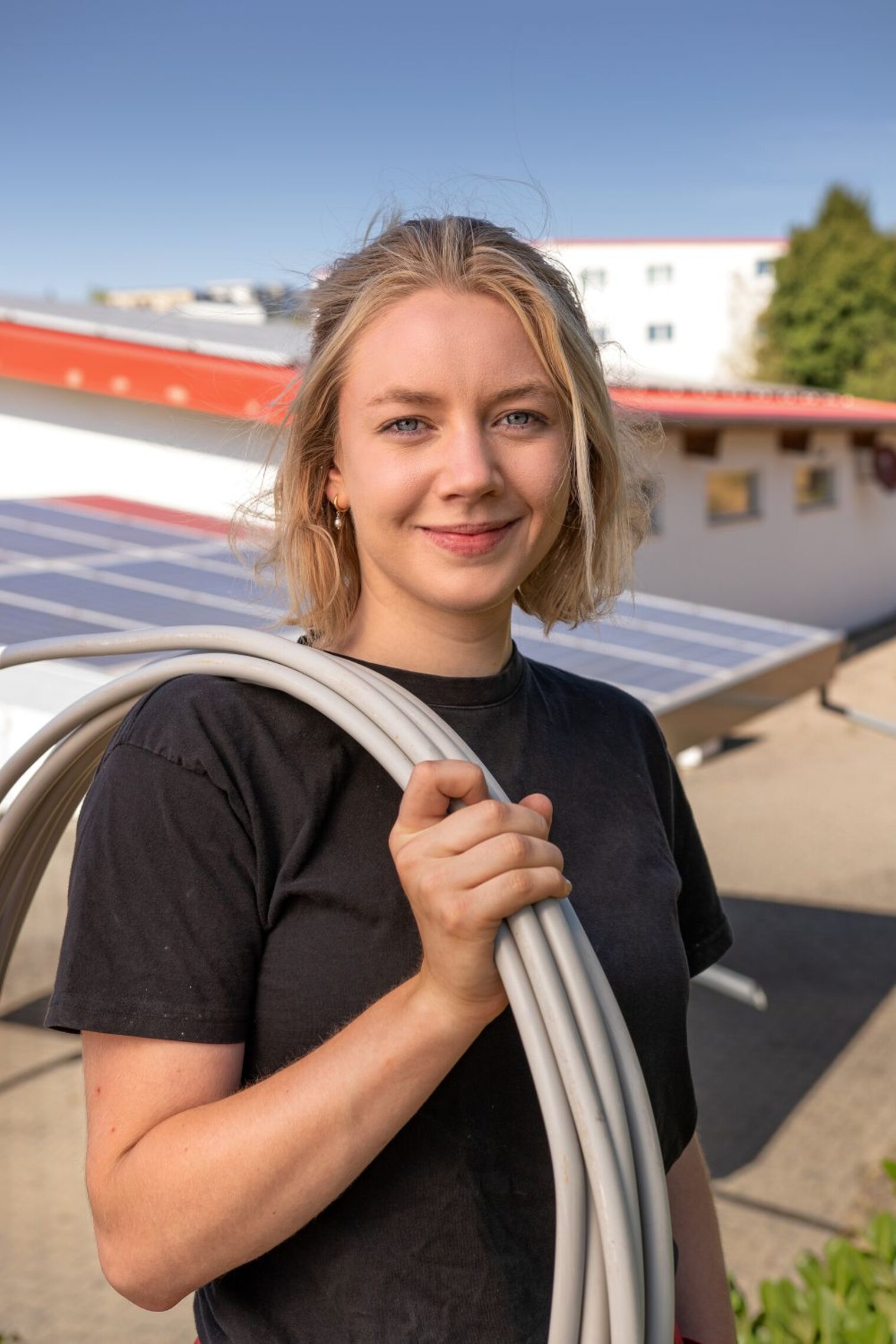 Annika Goebel mit zusammengerollten Kabeln über der Schulter lächelt in die Kamera