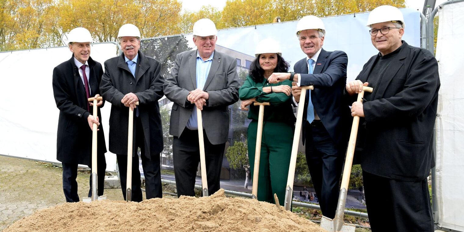 6 Personen aus HWK-Führungspitze und NRW-Ministerium posieren mit ihren Spaten an der Baustelle.
