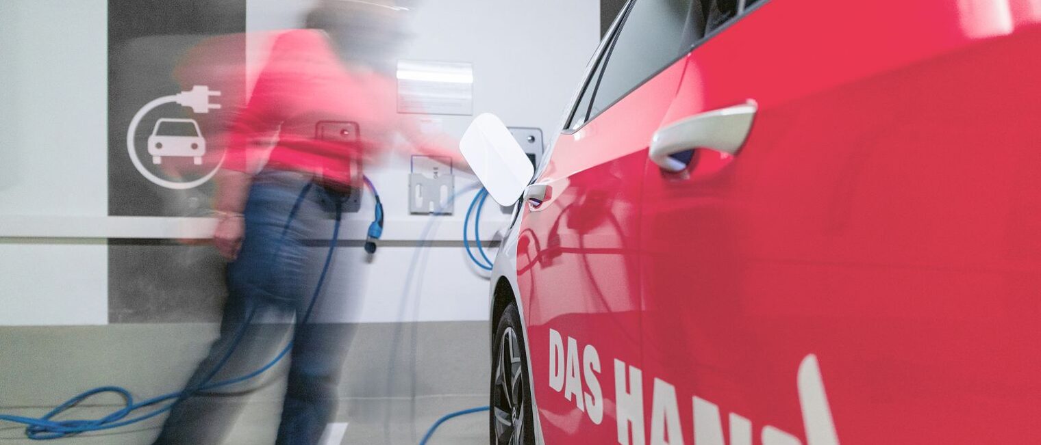 Eine Frau lädt einen PKW mit der Aufschrift "Das Handwerk" mit Strom auf.