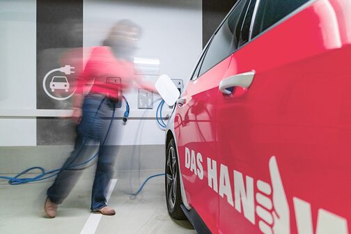 Eine Frau lädt einen PKW mit der Aufschrift "Das Handwerk" mit Strom auf.